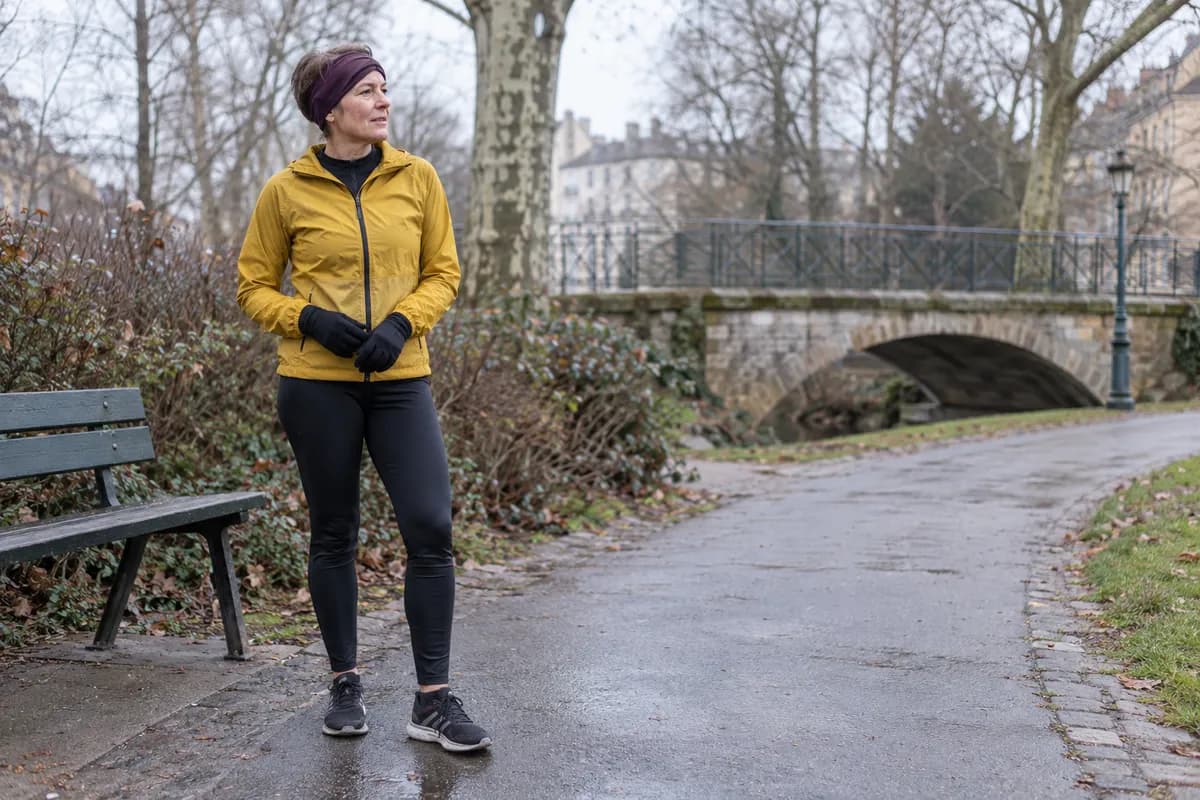 Runner wearing a wind jacket, tights, gloves, and a headband during a pause in the park