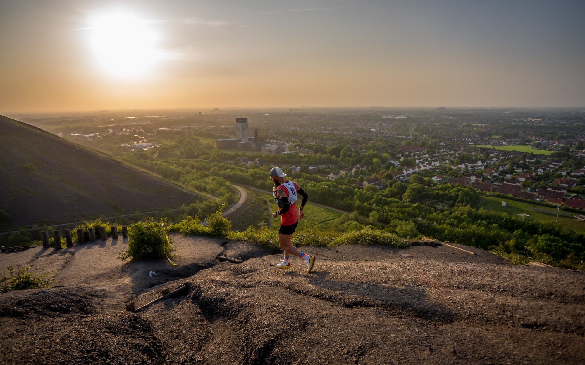 Runner on a hill path overlooking a city in low sunlight