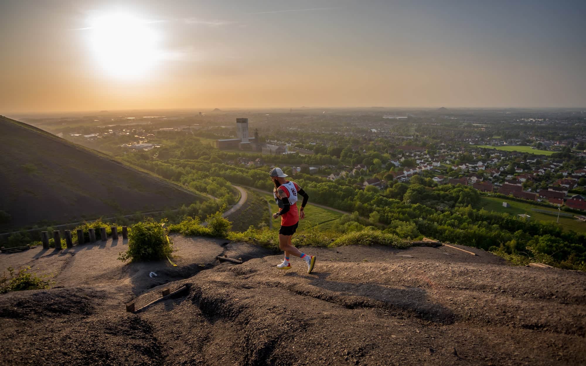 Runner on a hill path overlooking a city in low sunlight